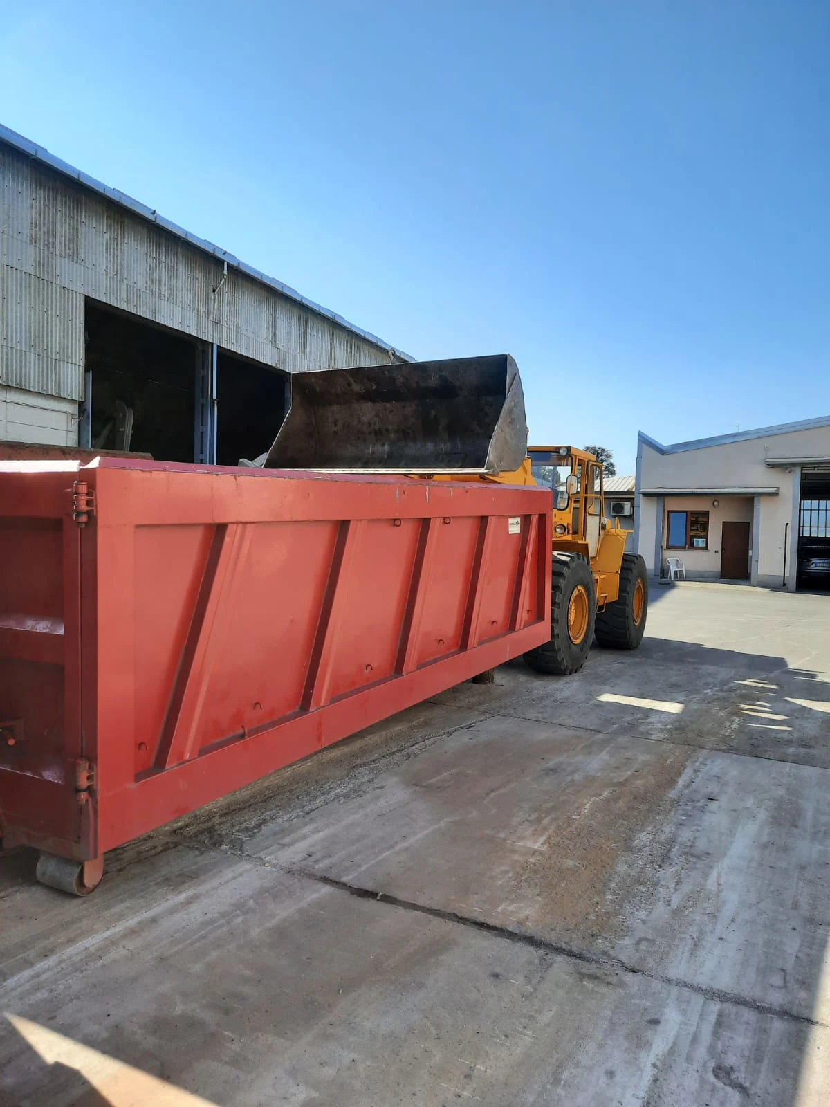 Container per rottami metallici caricato con pala meccanica in area industriale